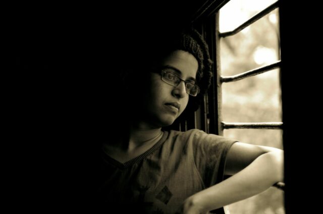 Person gazing out window in dim light.
